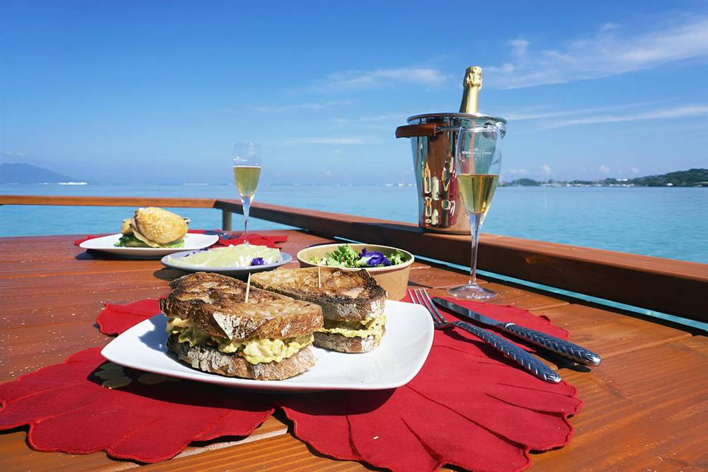 Dégustation à bord : sandwichs, salade et champagne sur la table en bois face au lagon
