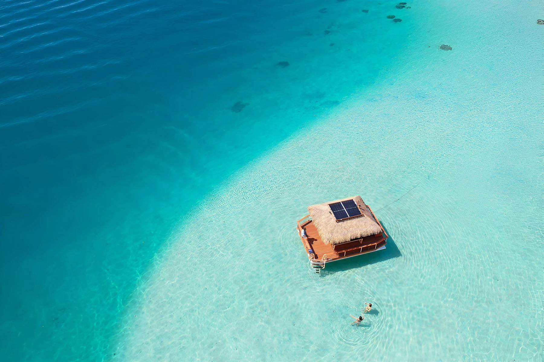 Vue aérienne du Vaimareva ancré sur le banc de sable turquoise du lagon de Punaauia, deux baigneurs à côté du bateau